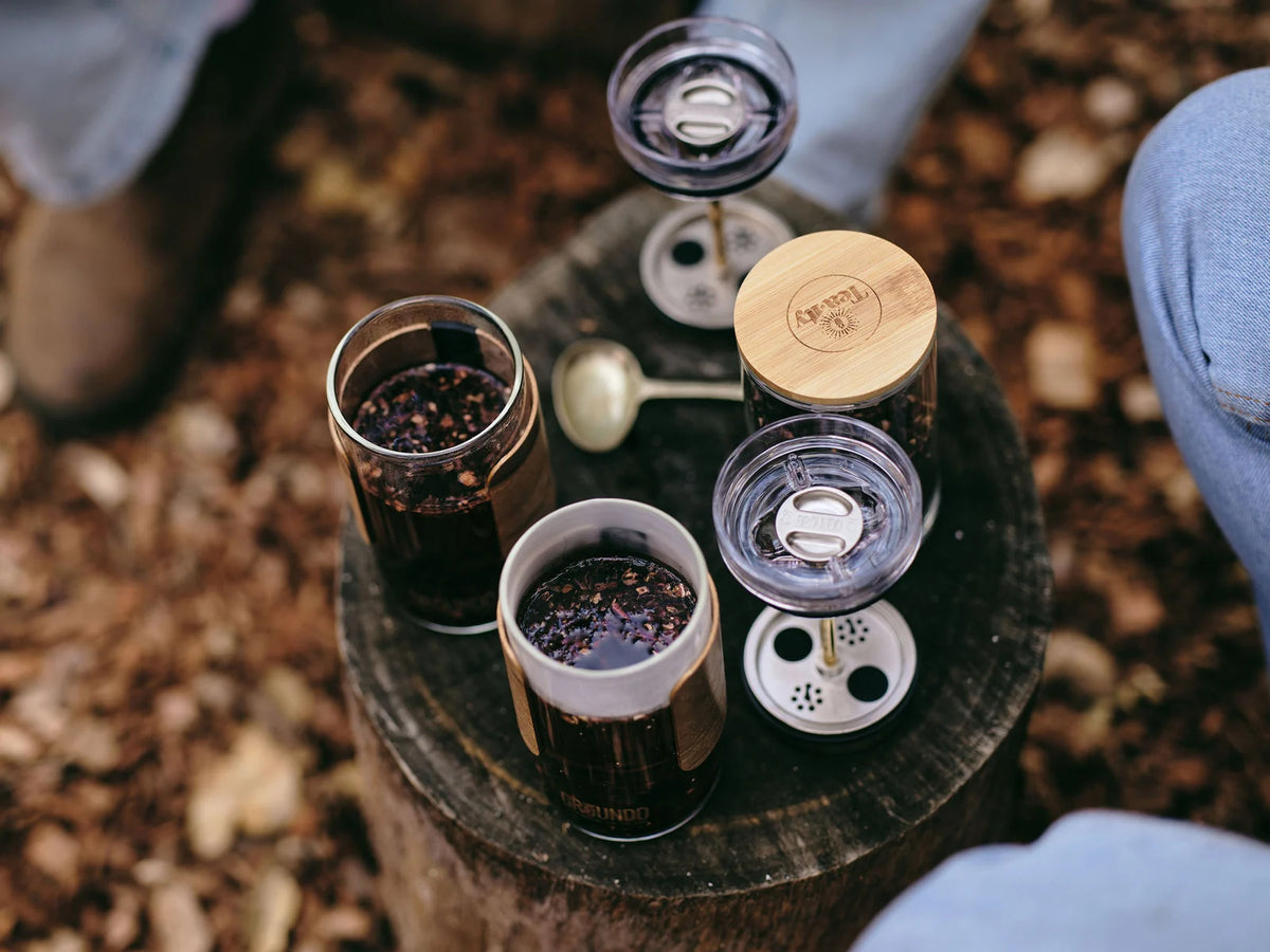 GROUNDD xpress components on a tree stump: two brewing cups, the lid assemblies, filters and brass shafts