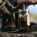 Hand pressing the GROUNDD xpress plunger, coffee brewed on a coastal rock