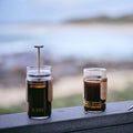 Two GROUNDD xpress cups resting on a rail above the coast