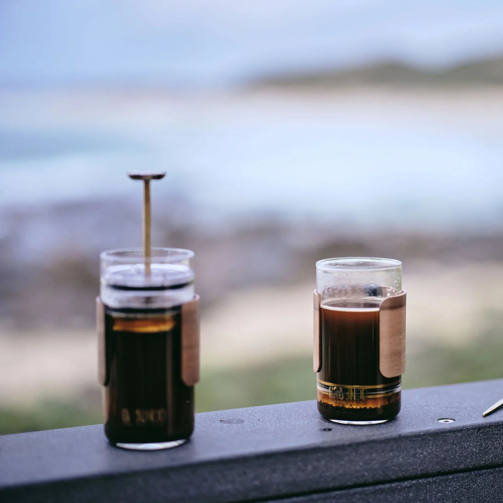 Two GROUNDD xpress cups resting on a rail above the coast