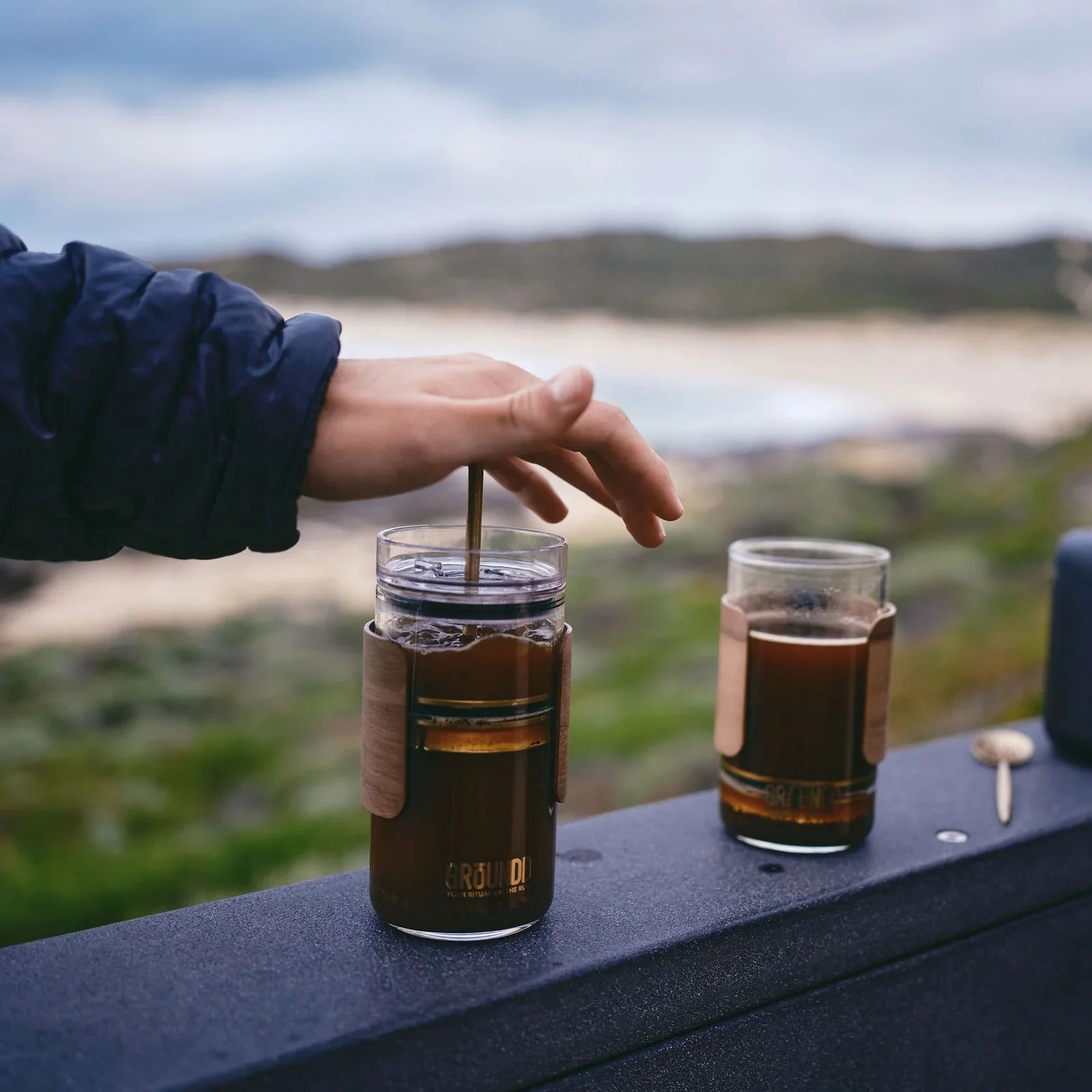Two GROUNDD xpress cups on a rail above the beach, one being plunged
